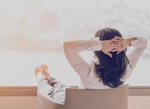 Back view of business woman sitting relaxing with legs raised and hands behind her head