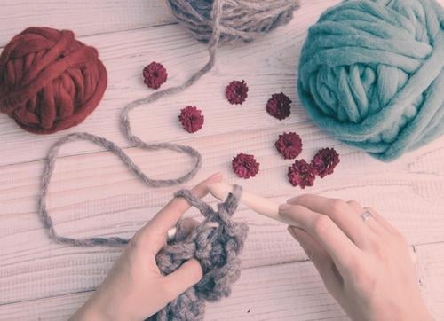 Balls of wool and maroon small flowers on a table and hands knitting