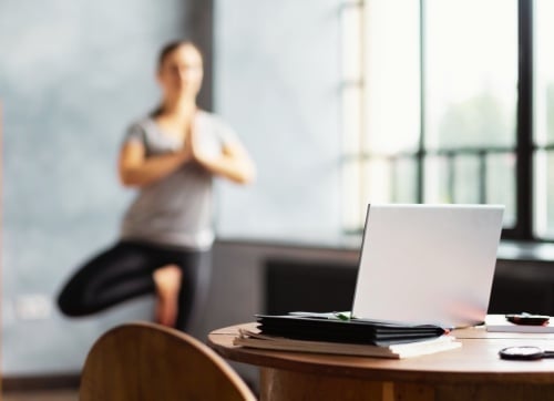 Blurred lady in the background doing yoga in her office, with a computer on a round table