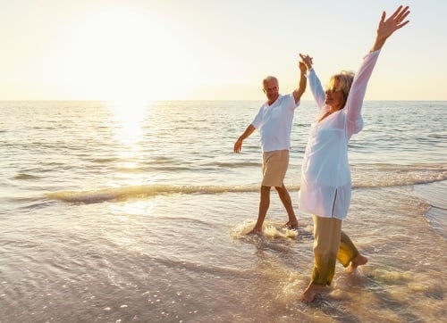 Elderly couple walking on the beach with bright sun in the backgroundlaxing  on the beach