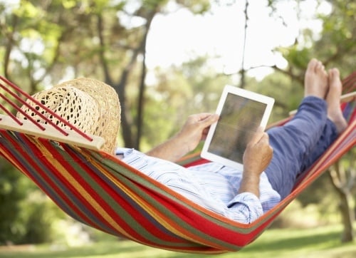 Elderly man relaxin in a hammock reading on a device