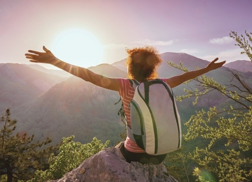 Image of back of Girl on top of a mountain with her arms open wide with the sun 