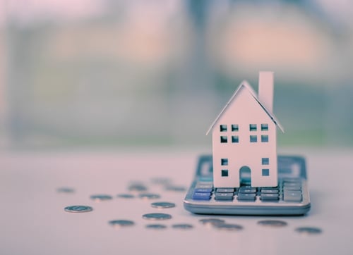 Paper house sitting on a calculator with coins scattered