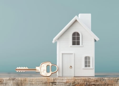 Small white toy house with an pastel green backdrop and a gold key