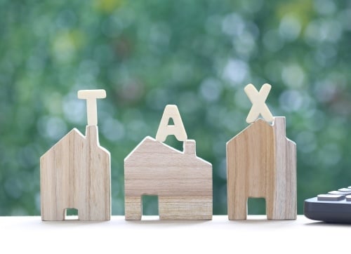 Three timber toy block homes with each letter of  TAX on each house, blurred tree background