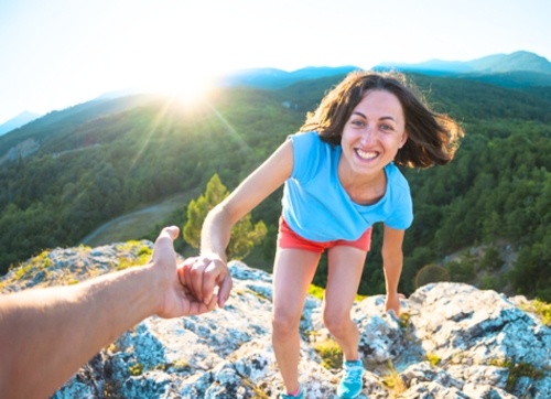 Woman getting a helping hand reach the top of a mountain