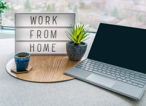 Work from Home sing on a desk with plant, coffee and laptop