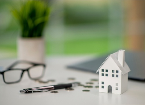 borrowing power -paper house, coins, glasses, pen laptop and plant