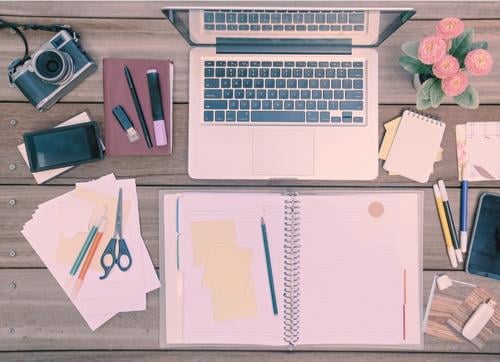 desk workspace with laptop, phone, camera, paper, scissors, flowers