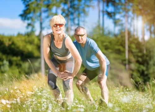 older couple in training gear stretching in a field before exercising