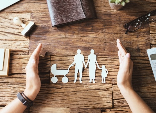 paper cut out of man, woman child and pram on a desk with hands cradling the cutout