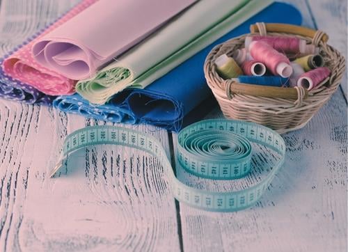 table top with measuring tap, cotton reels in a basket & material