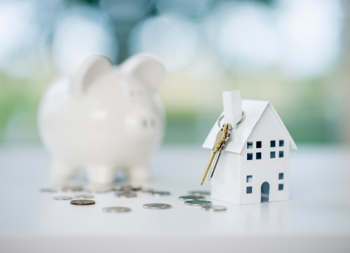 Pathway to wealth, white piggy bank and cardboard home with house keys