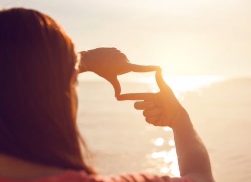 A woman holding her hands in a rectangle and capturing  sunrise over the ocean