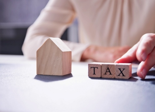 Man sitting behind a desk with a small timber block house and three timber blocks with tax written on them