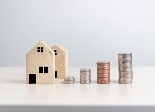 Two timber block toy houses with with piles of coins d