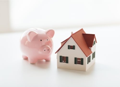 A pink piggy bank next to a miniature toy house