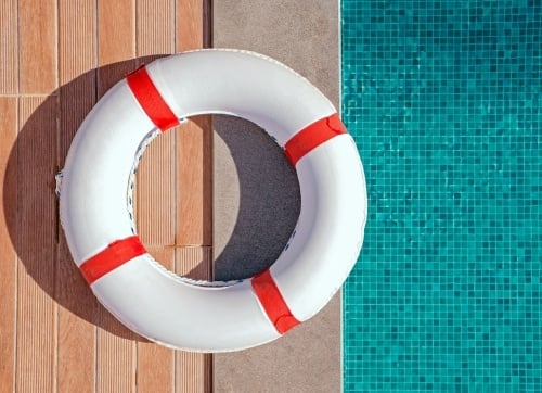 Red and white lifebuoy on the edge of a green mosaic tiled pool