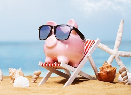 Pink ceramic piggy bank relaxing on a deck chair on the beach with sunglasses - enjoying his retirement