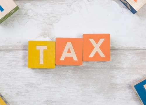 Three wooden blocks with the word TAX - one yellow block and two orange blocks