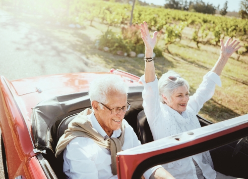 Elderly couple driving a red convertible through a vinyard