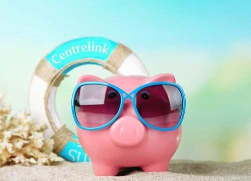 Pink piggy bank with blue sunglases standing on a beach with a lifesaving ring that says Centrelink